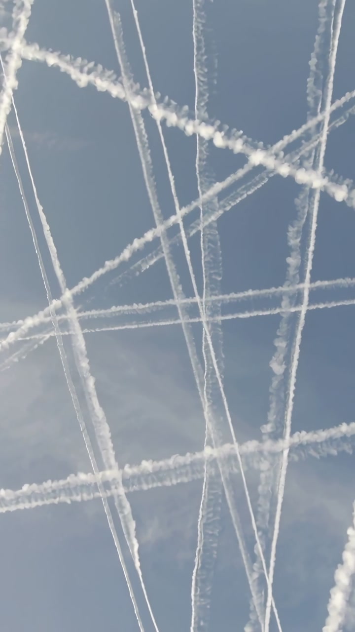 Vertical video: Forming contrails crossing blue sky after passing aircraft, spreading due to winds