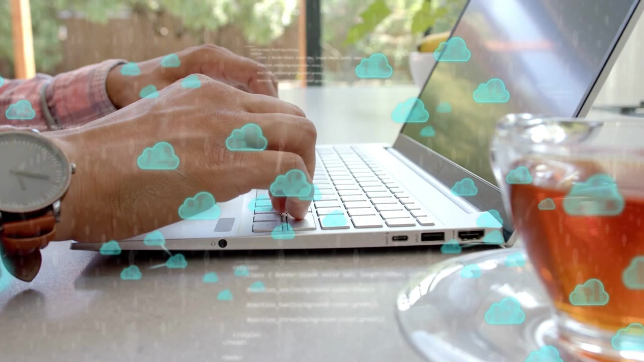 Lavoratore remoto che digita sulla tastiera accanto a una tazza da tè, generando icone di nuvole turchesi e sincronizzando i dati.