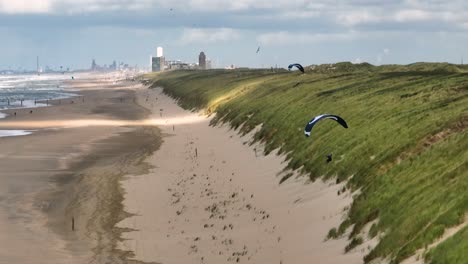 Toma-Aérea-De-Parapente-Volando-Sobre-La-Playa-De-Arena-Y-Las-Dunas-De-Los-Países-Bajos