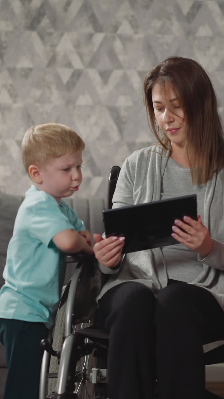 niño activo y preescolar distraen a la madre independiente del trabajo en la tableta. mujer con debilidad muscular habla con niños sentados en silla de ruedas