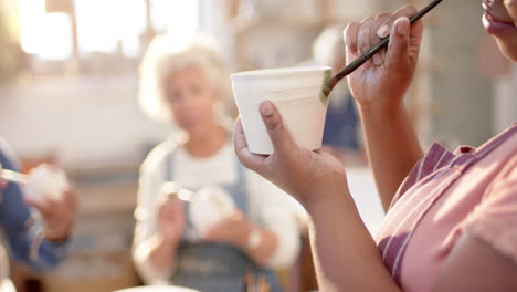 African-american-female-potter-with-braided-hair-glazing-clay-jug-in-pottery-studio,-slow-motion