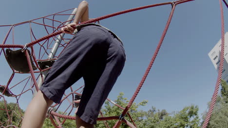 back view of focused boy climbing rope attraction on playground