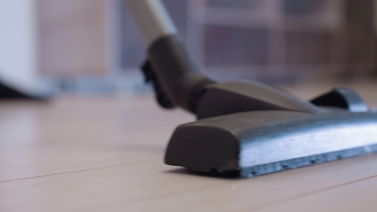 Close up of vacuum cleaner head moving across light wooden floor removing dust and dirt, concept of home hygiene, daily household chores, and modern cleaning routine with domestic equipment