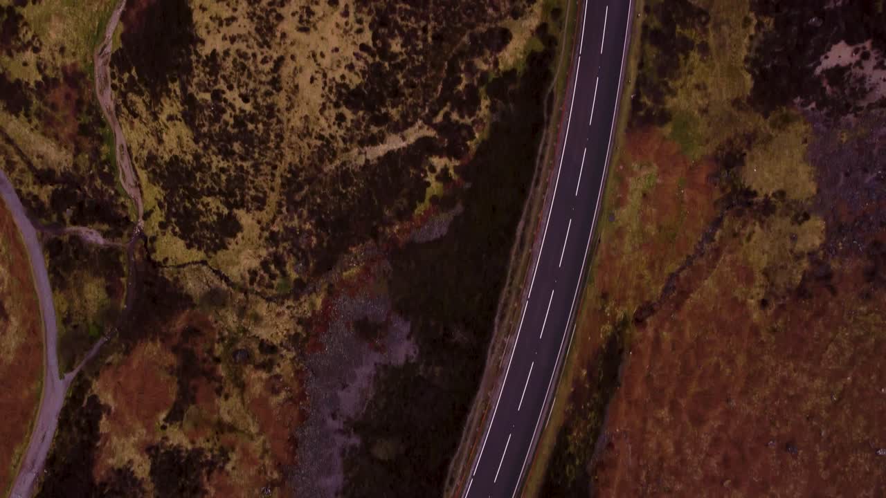 Una ripresa a volo d'uccello di una strada tortuosa nei Glens scozzesi che termina in un'area di sosta per roulotte la mattina presto di una fresca giornata estiva