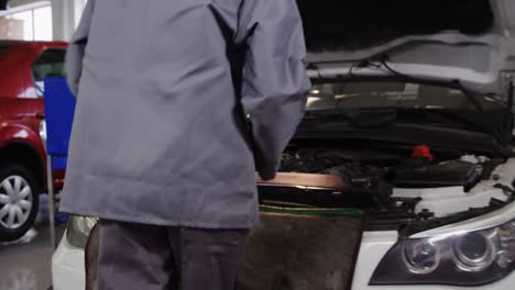 female mechanic using computer while servicing a car engine