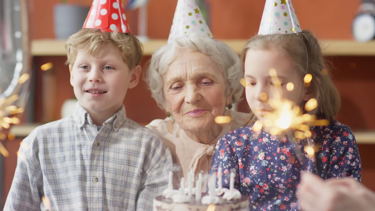 пожилая женщина дует свечи на торте с внуками