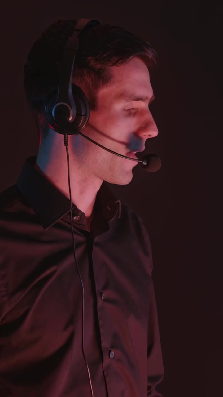 Vertikal video: Mann i svart skjorte med headset som trykker på det, vender seg og snakker inn i mikrofonen i et studio for lydopptak