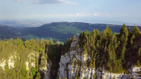 flying over mountain peek with green pines in switzerland showing a little town in the valley