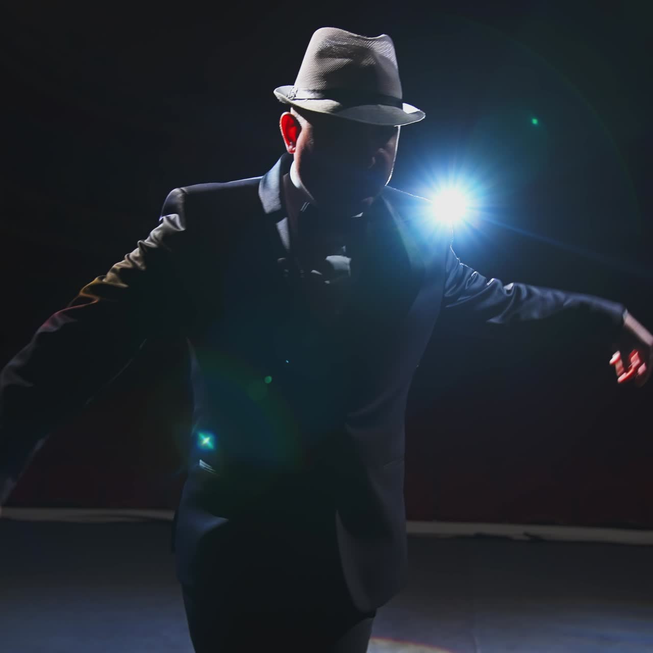 Male actor performing in the theater. Funny man putting on white hat and began dancing on stage in dark light. View from the stage.