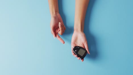 video of biracial woman using glucose meter on blue background