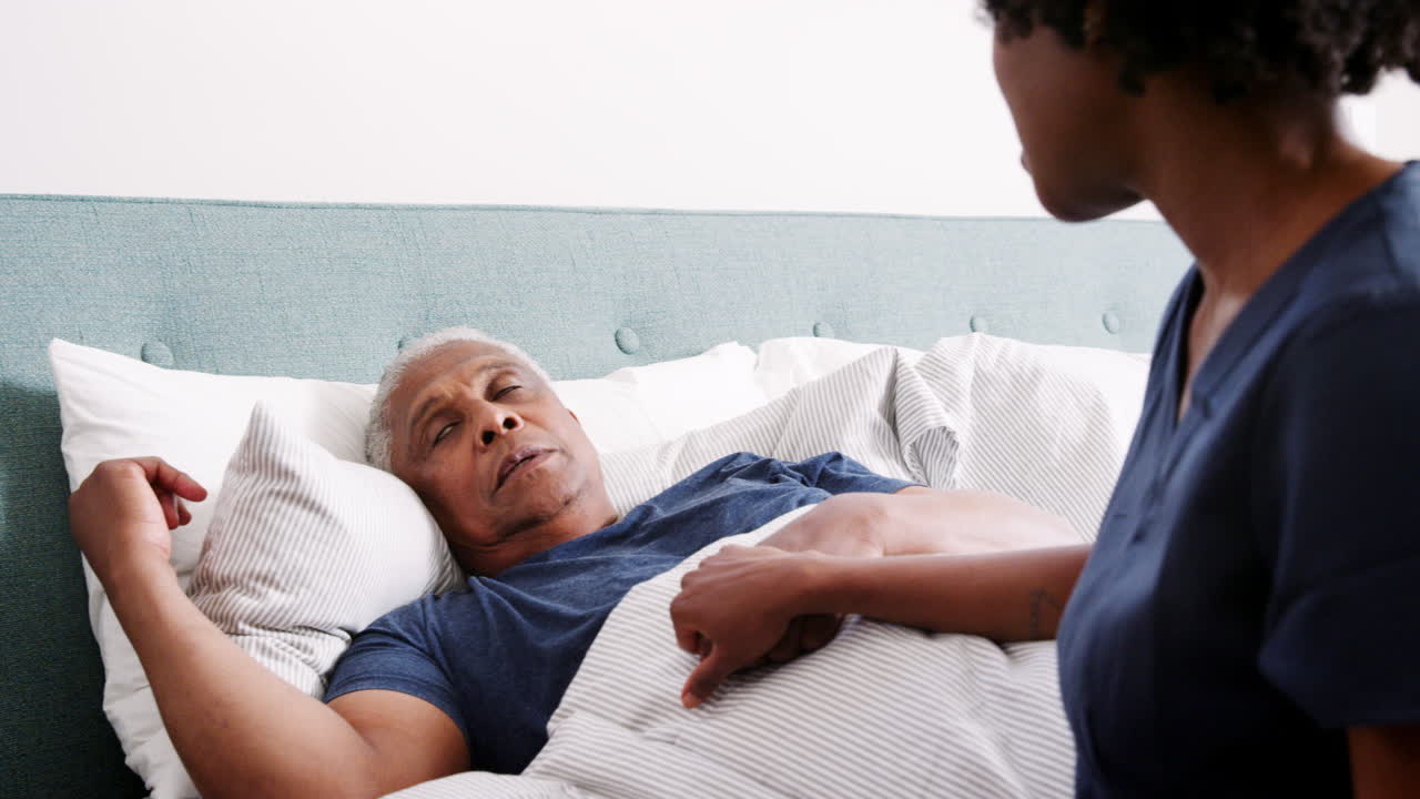 Nurse Visiting Senior Man Lying In Bed Suffering With Depression