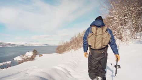 Man-With-A-Fishing-Rod-Walks-Alone-In-Deep-Snow-Towards-The-Shore-In-Trondheimsfjord,-Trondheim,-Norway