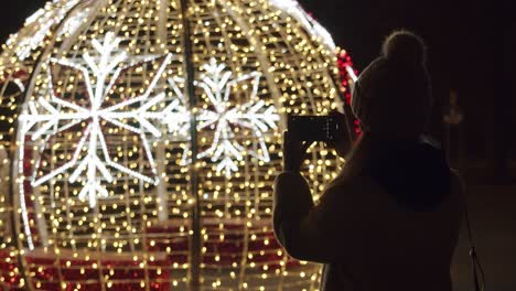 woman taking pictures with a phone of a christmas lights at night