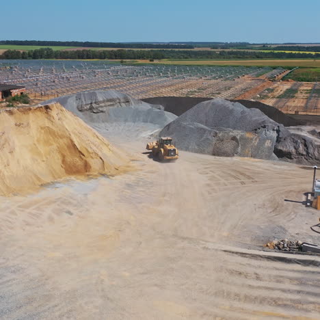 excavator on the quarry. big territory of asphalt factory. piles with sand and rubbles outdoors. aerial view. camera motion up.