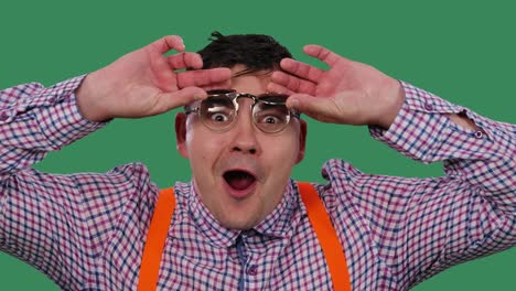 the man in the sunglasses lifts the tinted lenses with an enthusiastic expression on his face, says wow. portrait of a man in glasses in the studio on a green screen. slow motion. close up