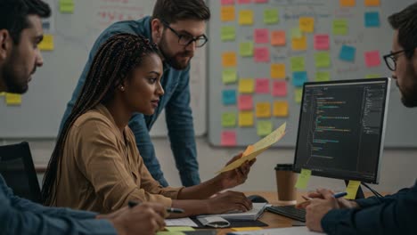 collaborative teamwork in a modern workspace: analyzing code and discussing solutions with post-it notes and laptops in a creative environment