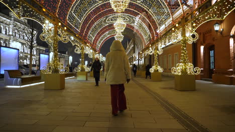 woman walking in moscow street under christmas lights wearing thick coat, rear follow