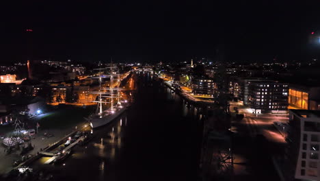 night view of a city harbor with a tall ship