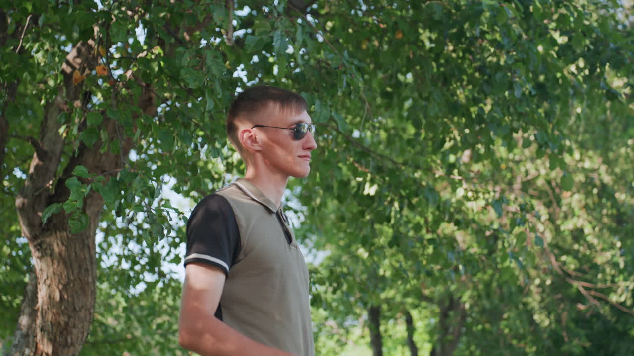 Youthful Gaze Upward, Man Examines Sky Through Foliage, Youthful Individual Glances Through Leaves With Thoughtful Expression, Young Man Lifts Glasses To Observe Sky Beneath Tree Canopy Gracefully
