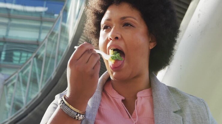 Plus size biracial woman eating salad in city