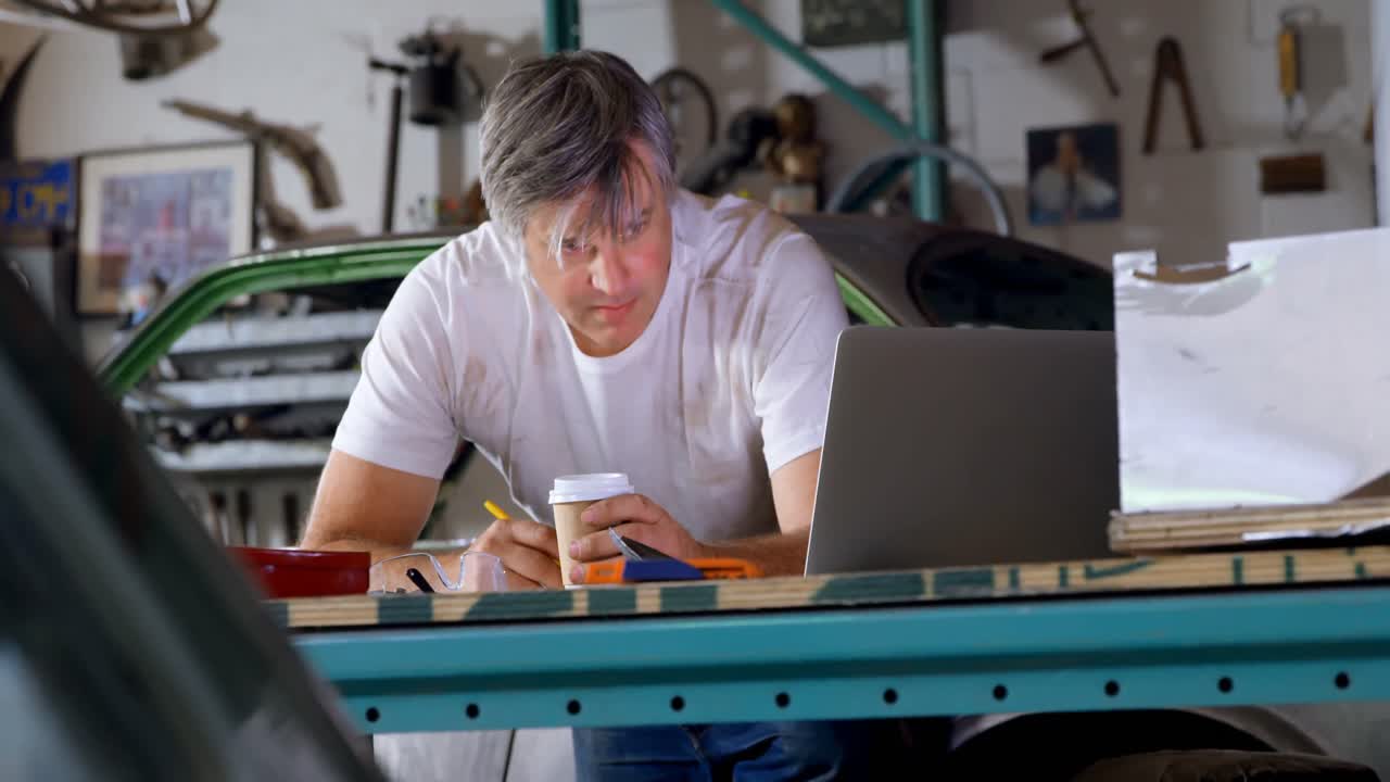 Mandlig mekaniker, der drikker kaffe, mens han skriver ved et bord 4k