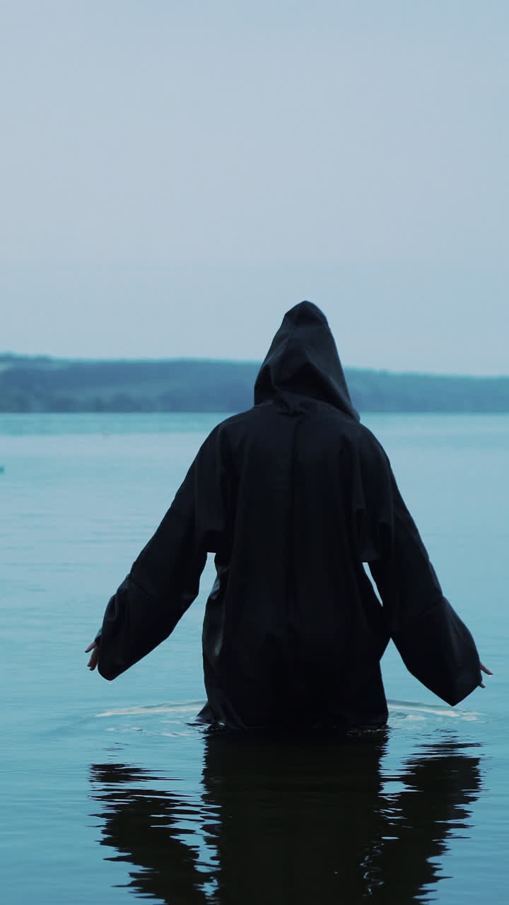 Scary figure in black mantle in the river. Halloween costume. Vertical video