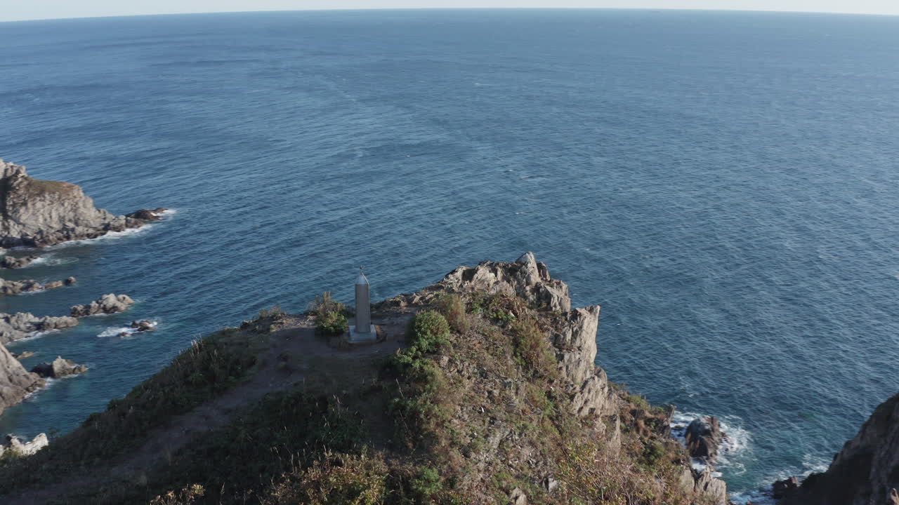 toma de pivote aéreo de un monumento, instalado en lo alto de un acantilado rocoso y empinado, con una bahía rocosa al fondo, al atardecer