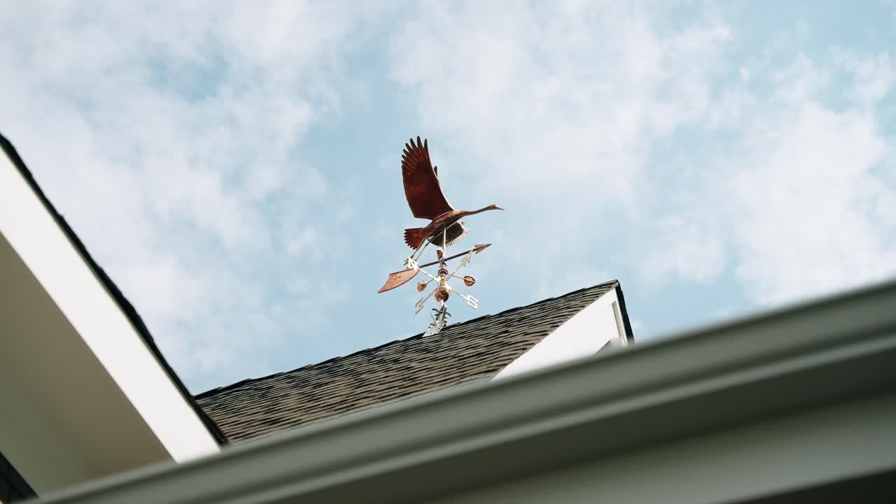 Bronze wind vane on top of a luxury home on a partly cloudy day