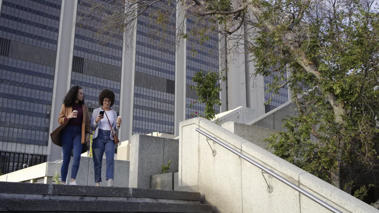 Amigas diversas suben las escaleras de una plaza después de saludarse, comparten el teléfono y beben café.