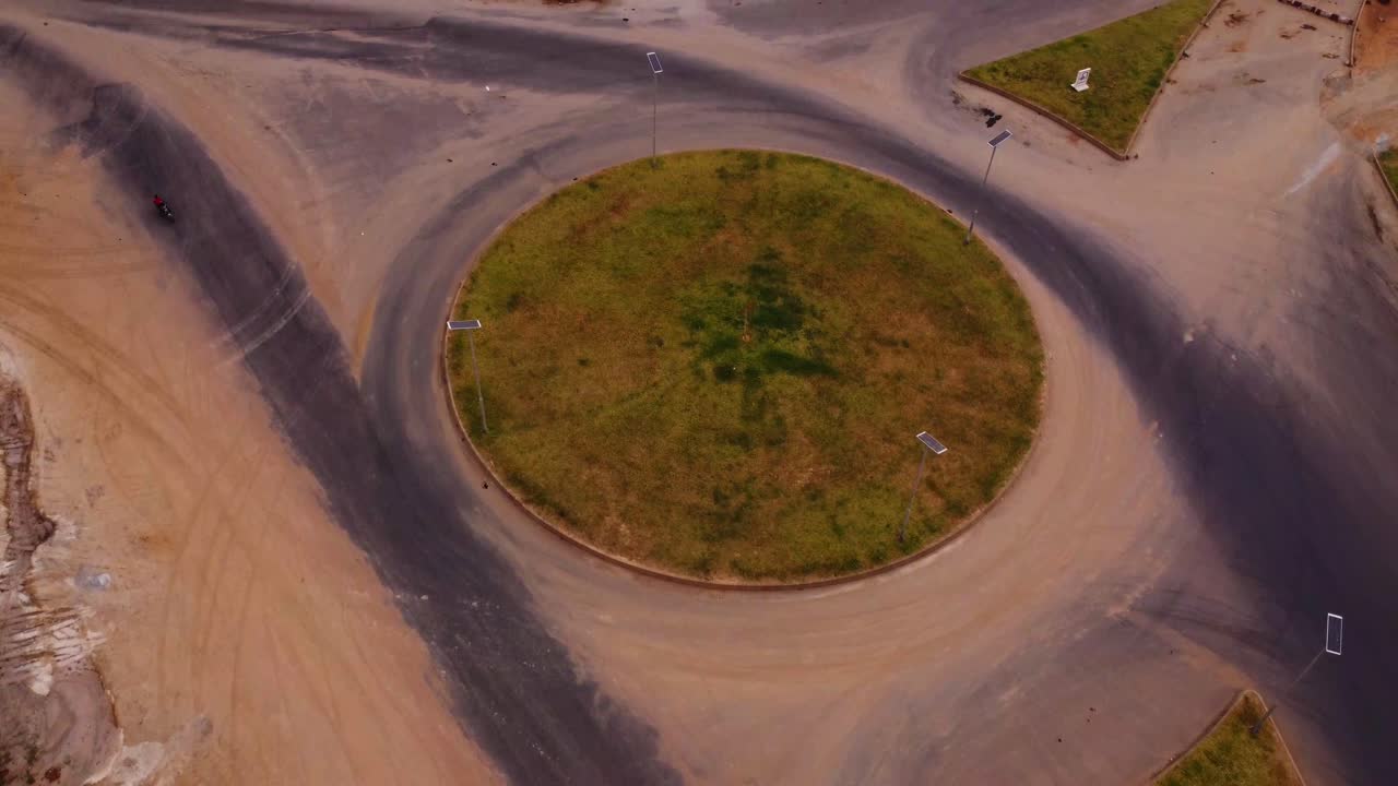 Jib down of a large roundabout in rural Nigeria with a single motorcycle driving over the calm road