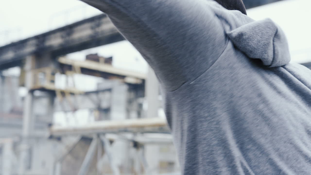 흐린 아침에 버려진 공장 밖에서 샌드백을 때리는 운동복을 입은 백인 남자의 뒷모습