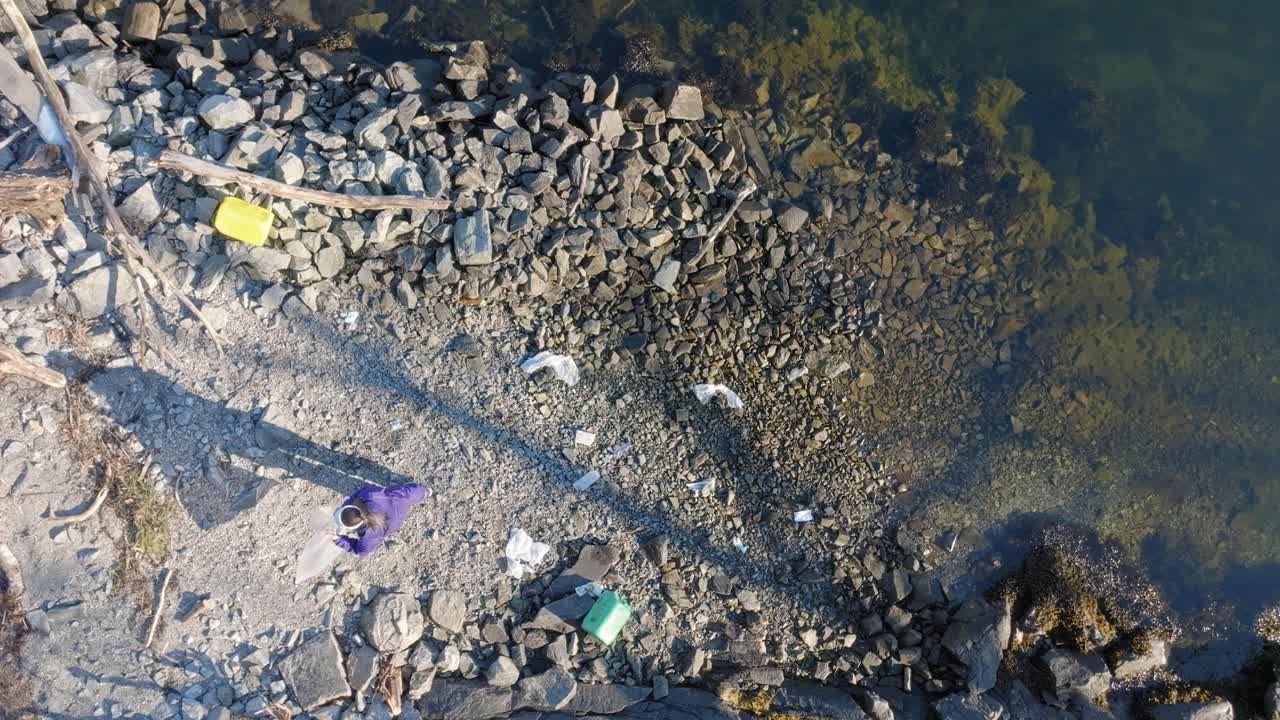 вид с высоты птичьего полета женщины, собирающей пластиковые отходы со скалистого берега норвегии