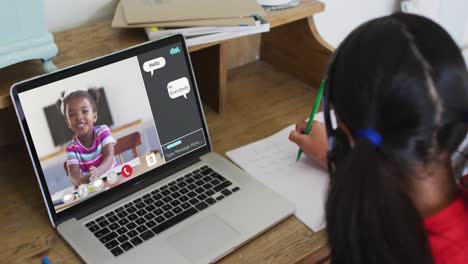 Schoolgirl-using-laptop-for-online-lesson-at-home,-with-girl-talking-and-web-chat-on-screen