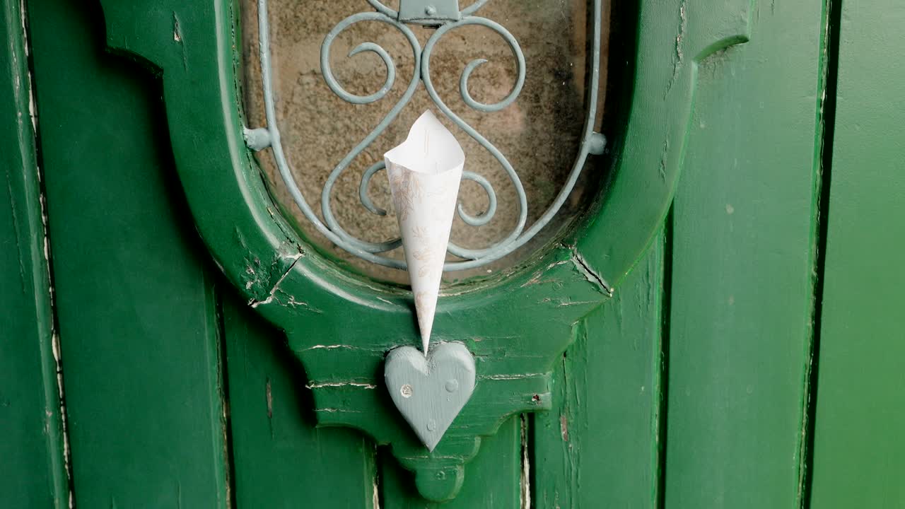 close up of paper cone in heart shaped holder on vintage green wooden door with iron detail