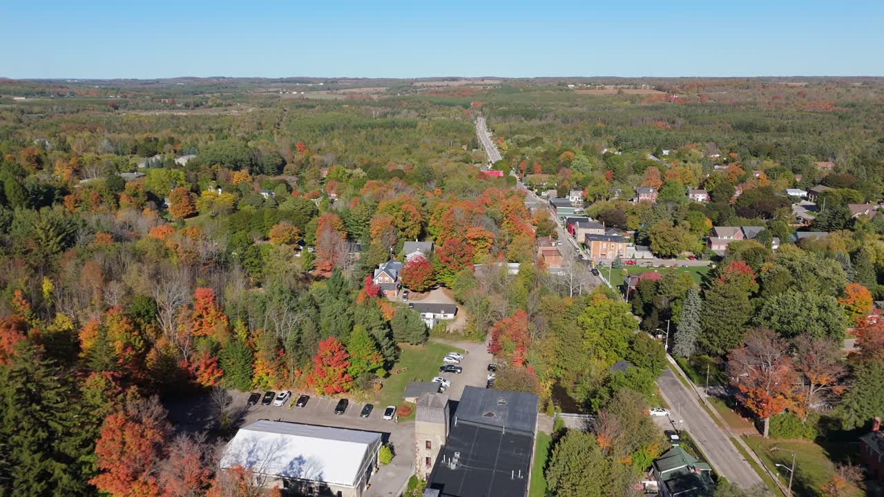 A beautiful drone shot of the historic Alton Mill Arts Centre, nestled beside a millpond and enveloped by a forest of vibrant fall foliage in rural Ontario, Canada