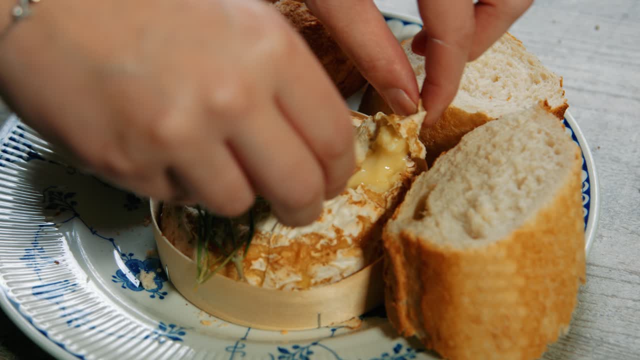Hand Breaking and Dipping Baguette in Freshly Baked French Camembert Cheese