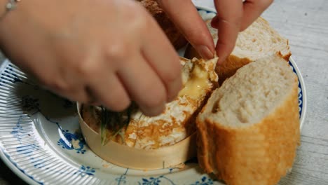 hand breaking and dipping baguette in freshly baked french camembert cheese