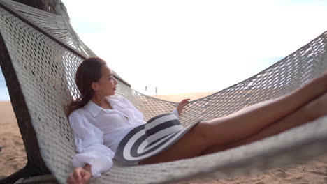 asian woman relaxing lying in a beach hammock under tree