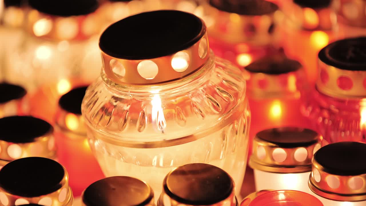 Sharp focus on burning glass jar candle surrounded by soft orange and red glow
