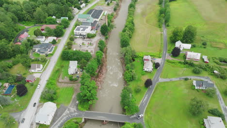 wide aerial drone view: raging river with edge debris in flood-impacted vermont