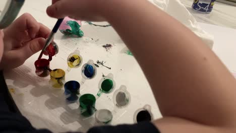 close-up. the boy is playing with the paint at the table. he wipes the brush into a white handkerchief