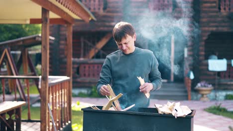 Ein-Reisender-Junger-Mann-Steht-In-Der-Nähe-Des-Grills,-In-Dem-Vor-Dem-Hintergrund-Drei-Kohlen-Rauchen