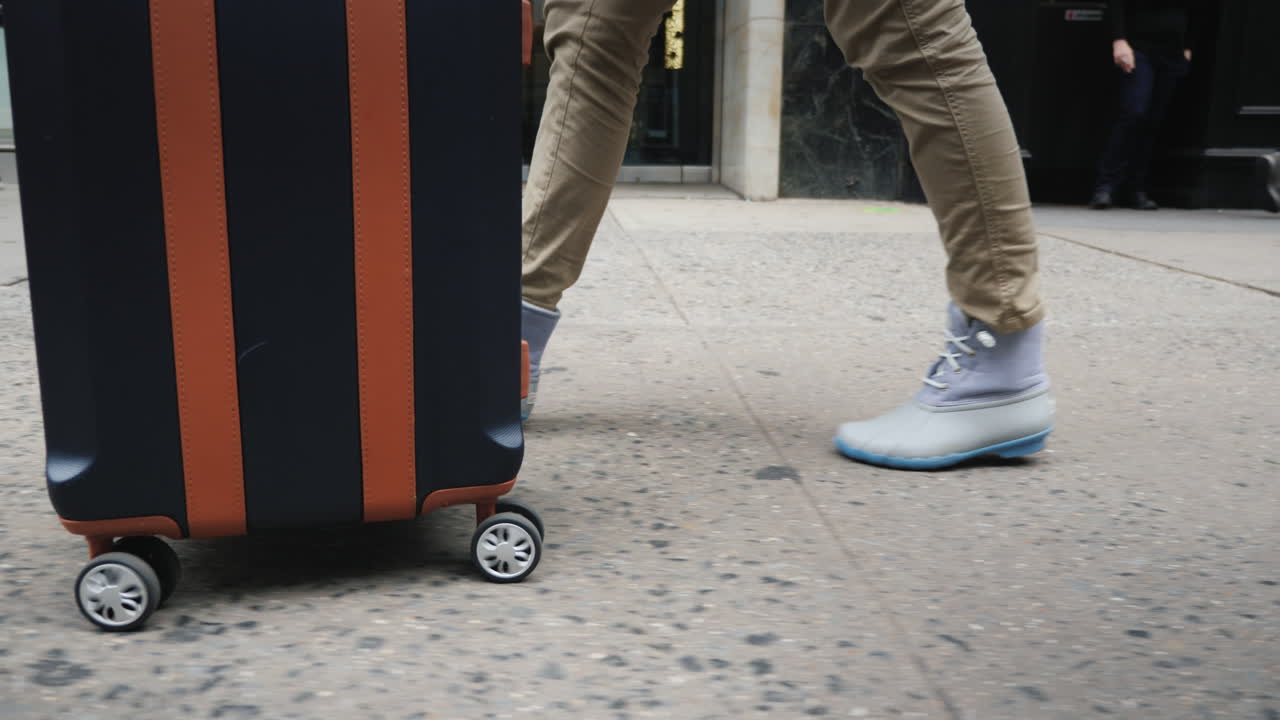 una mujer con una bolsa de viaje sobre ruedas va a un paso de peatones en una multitud de personas que solo tienen piernas