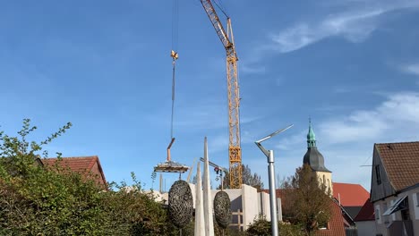 Huge-crane-lifting-wooden-pallet-down-on-sunny-day-with-blue-sky,wide-shot