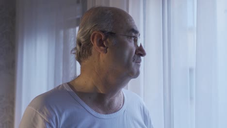 A-pensive-old-man-sitting-alone-at-home-is-looking-out-the-window.