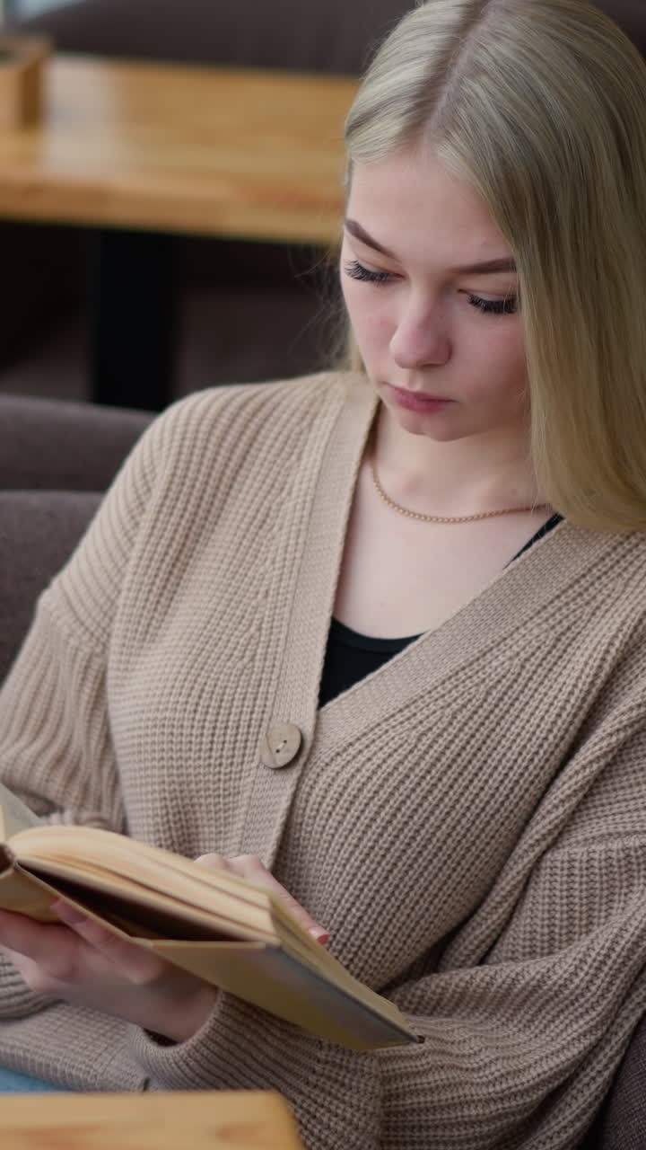 Eine Frau sitzt bequem und entspannt, während sie ihr Buch liest, vertieft in ihre Lesesitzung, in einem gemütlichen Lernbereich mit einer warmen Kaffeetasse auf dem Tisch.