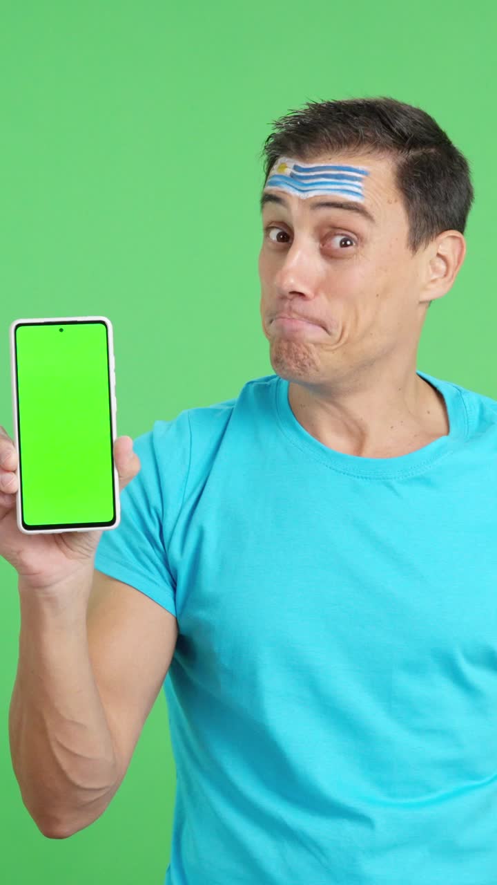 Uruguayan supporter looking at his mobile smiling and showing it