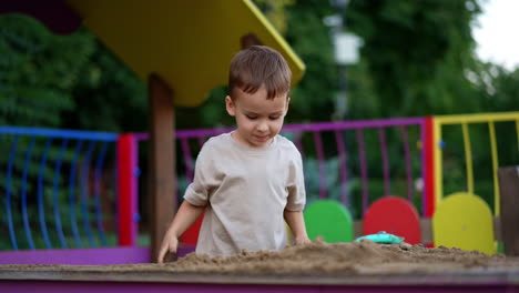 adorable joyful toddler tapping his hands by the sand. lovely caucasian kid playing in the sandbox outdoors.