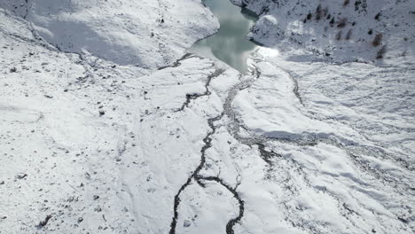 drone-view-of-the-delta-of-a-frozen-glacier-river-in-the-Alps-from-a-Drone-in-Winter-on-a-sunny-day,-Italy