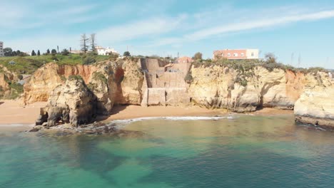 Playa-De-Pinhão-Cala-Tranquila-Con-Pintorescas-Aguas-Cristalinas-Rodeadas-De-Acantilados-En-Lagos,-Algarve-Portugal---Toma-De-Seguimiento-De-Establecimiento-Amplio-Aéreo